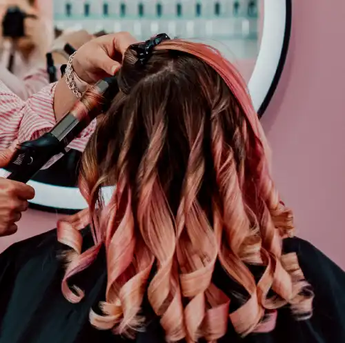 hairdresser styling a client's curls with a curling iron in salon in Staines