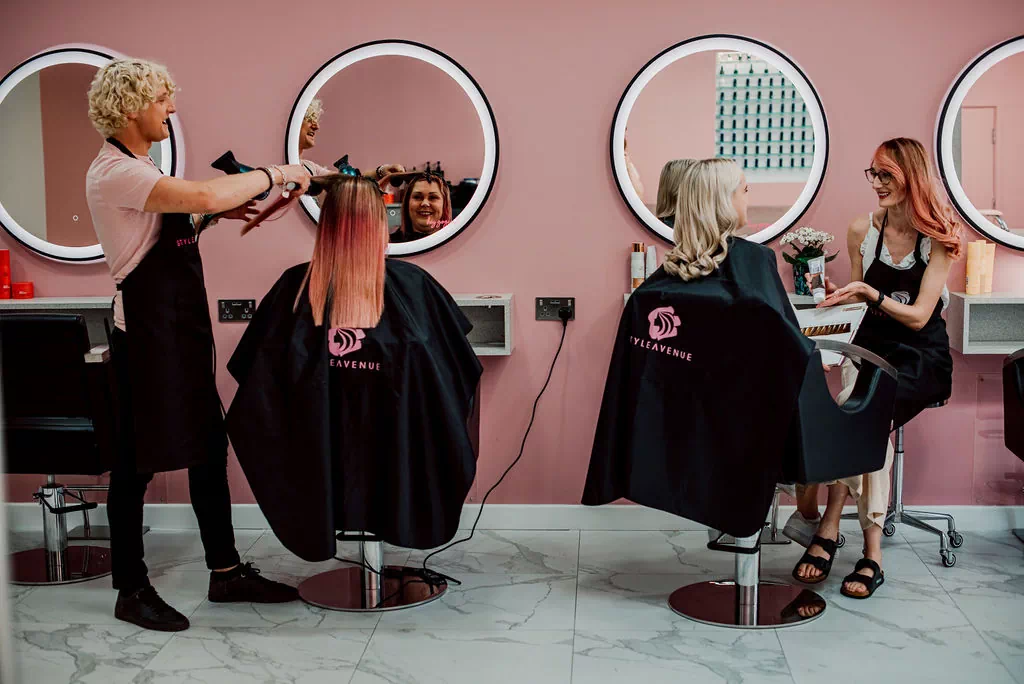 hairdresser drying a client's hair and a hairdresser presenting a hair product to a client